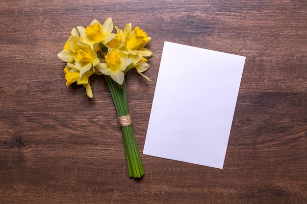 Een boeket van narcissen en een vel wit papier op een houten achtergrond