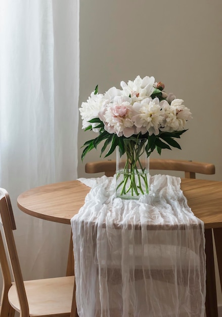 Een boeket van prachtige witte pioenrozen in een glazen vaas op een houten ronde tafel met een wit tafelkleed