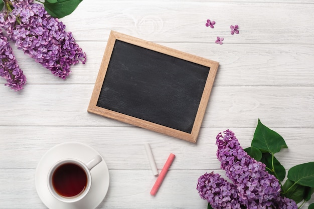 Een boeket van seringen met een kopje thee, krijtbord op witte planken