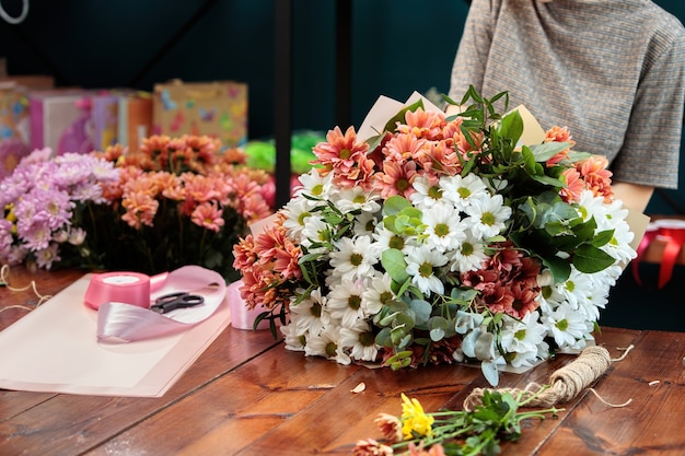 Een boeket van veelkleurige chrysanten ligt op een houten tafel. Het proces van het maken van een boeket bloemen door een bloemist.