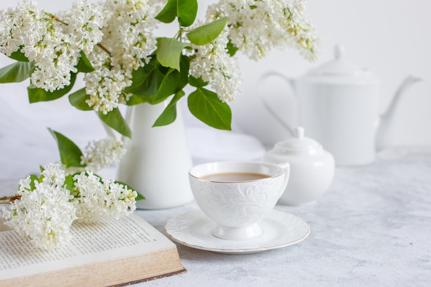 Een boeket van witte lila, een kopje koffie en een oud boek