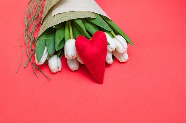 Een boeket van witte tulpen en een rood fluwelen hart op een rode tafel - het concept van Valentijnsdag.