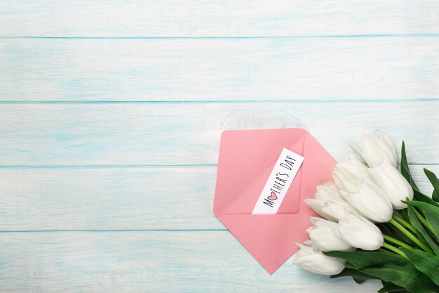 Een boeket van witte tulpen met een liefdesbrief en kleur envelop op blauwe houten planken. moederdag