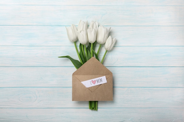 Een boeket van witte tulpen met liefdesbrief en envelop op blauwe houten planken. moederdag