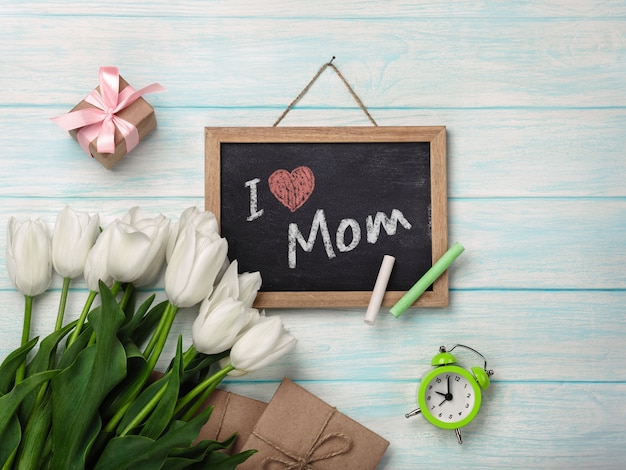 Een boeket van witte tulpen met schoolbord, enveloppen van de geschenkverpakking op blauwe houten planken. Moederdag