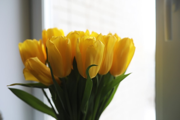 Een boeket verse gele tulpen in een vaas op een tafel bij het raam