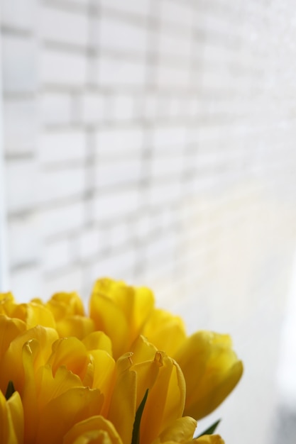 Een boeket verse gele tulpen in een vaas op een tafel bij het raam