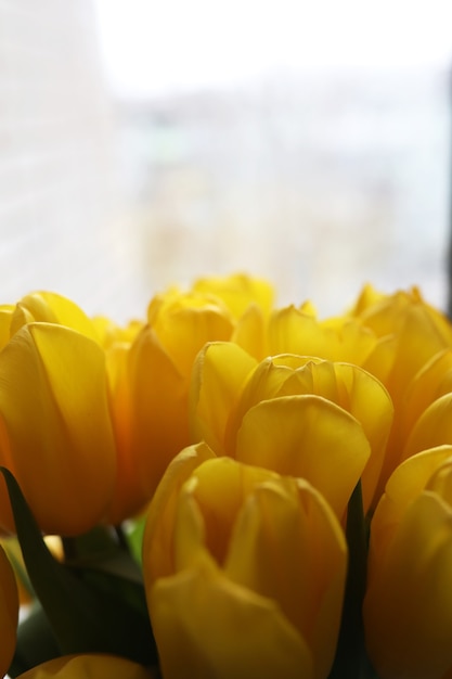 Een boeket verse gele tulpen in een vaas op een tafel bij het raam