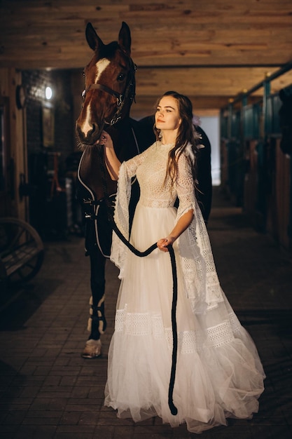 Een boho-bruid poseert met een paard in een stal