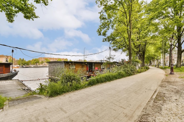 Een boot aangemeerd aan de kant van een rivier naast enkele bomen en gebouwen op de achtergrond is een blauwe lucht met witte wolken