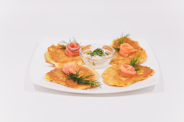 Een bord aardappelpannenkoekjes versierd met basilicumbladeren op de tafel.