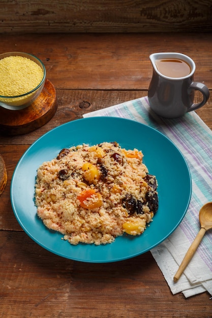 Een bord couscous met gedroogde vruchten en noten op een houten tafel naast de ingrediënten