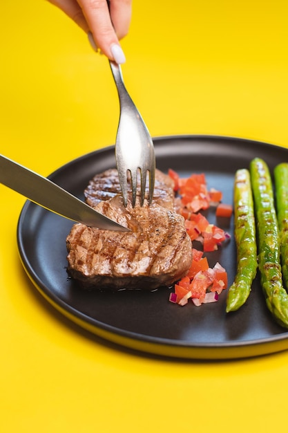 Foto een bord eten met een in stukjes gesneden biefstuk en een mes wordt boven een bord met asperges gehouden.