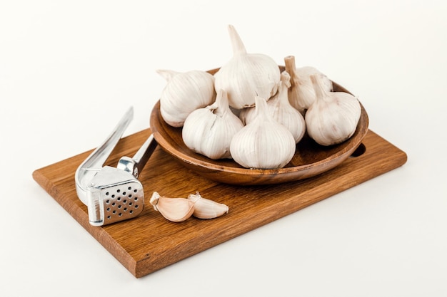 Een bord knoflook met knijp- en snijplank geïsoleerd op een witte achtergrond.