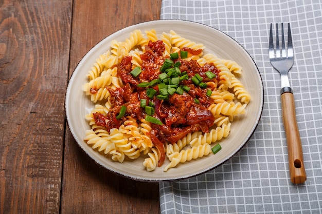 Een bord met bolognese pasta op een houten tafel naast een licht servet en een vork