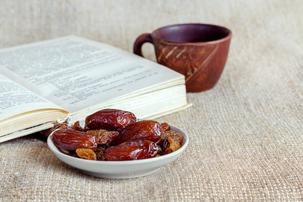 Een bord met dadels en rozijnen bij een kopje koffie en een open boek