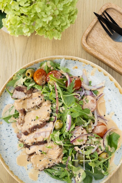 Een bord met kalfsvlees op groenten met groenten en olijven onder notensous op een houten tafel.