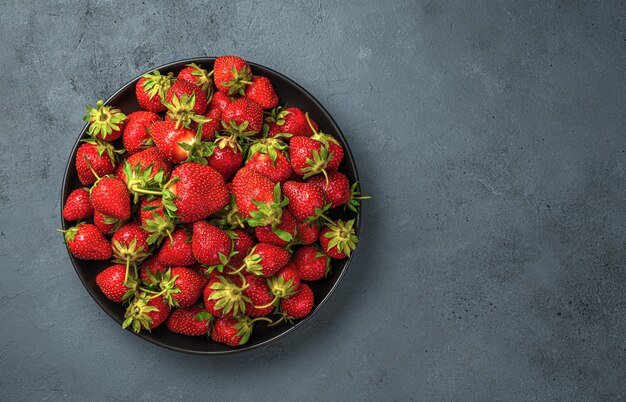 Een bord met rijpe aardbeien op een donkerblauwe achtergrond. Bovenaanzicht, kopieer ruimte.