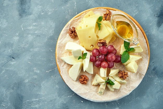 Een bord met verschillende kazen geserveerd met druiven, noten en honing. Voorgerecht Kaasplaat. Gesneden Camembert, Brie, Parmezaanse Blauwe Kaas