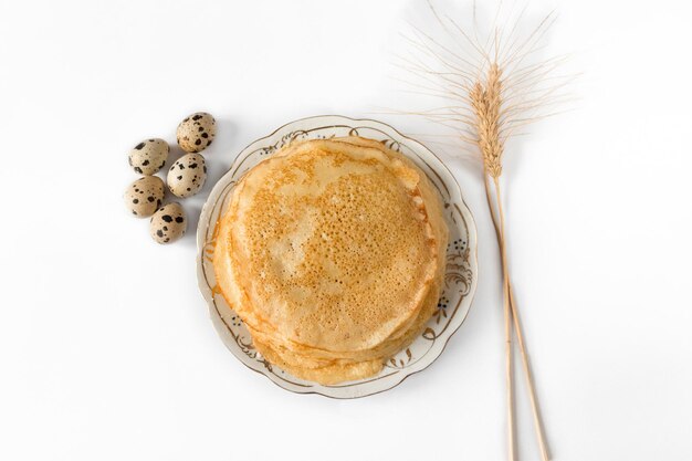 Een bord pannenkoeken met kwarteleitjes en een spica op een witte achtergrond. Maslenitsa-concept. Selectieve aandacht.