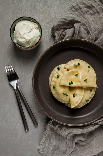 Een bord ravioli met een kom zure room ernaast.