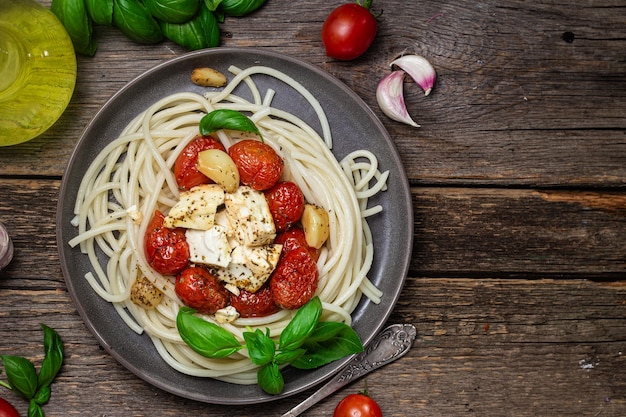 Een bord spaghetti met tomaten, kaas en basilicum op een houten tafel.