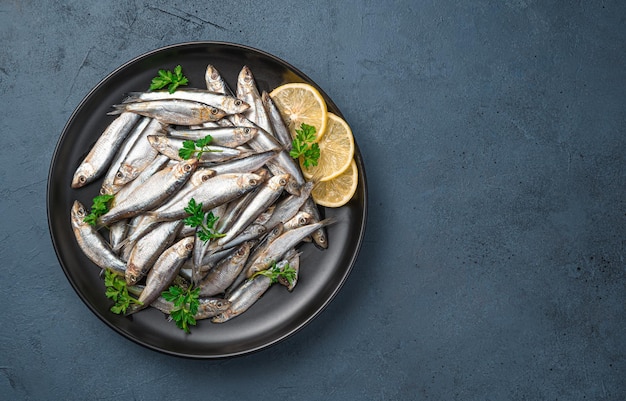 Een bord vol sardines met citroen en peterselie op een donkerblauwe achtergrond. Bovenaanzicht, kopieer ruimte. Zeevis.