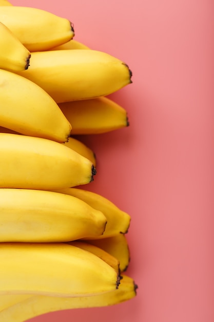 Een bos van rijpe gele bananen op een roze achtergrond.