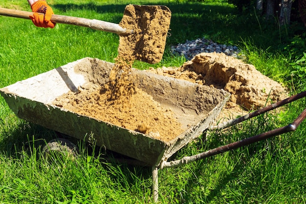 Een bouwmeester giet zand in een kar met een schop om beton te maken