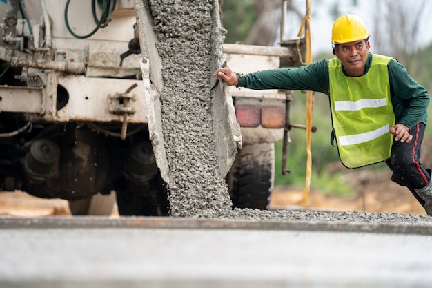 Een bouwvakker die een natte concret giet bij wegenbouwplaats