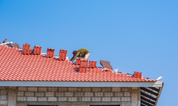 Een bouwvakker legt oranje dakpannen op het heupdak van een modern huis