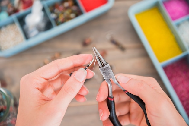 Een bovenaanzicht van een vrouw tot vaststelling van de oorbel haak met tang op houten bureau