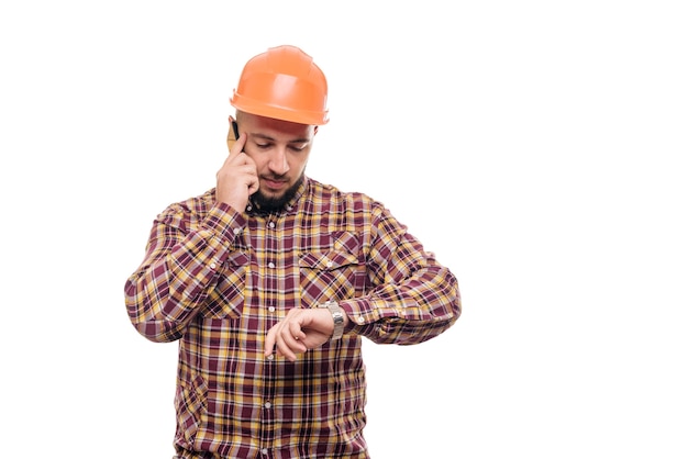 Een boze en nerveuze arbeider met een oranje helm praat luid aan de telefoon, schreeuwt in de telefoon. Geïsoleerde witte achtergrond