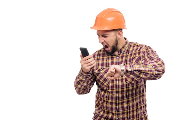 Een boze en nerveuze arbeider met een oranje helm praat luid aan de telefoon, schreeuwt in de telefoon. Geïsoleerde witte achtergrond