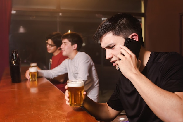 Een boze jongeman maakt ruzie aan de telefoon terwijl zijn dronken vrienden aan de bar genieten van een biertje.