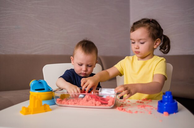 Een broer en zus spelen aan een tafel met kinetisch zand. Raak games thuis aan.