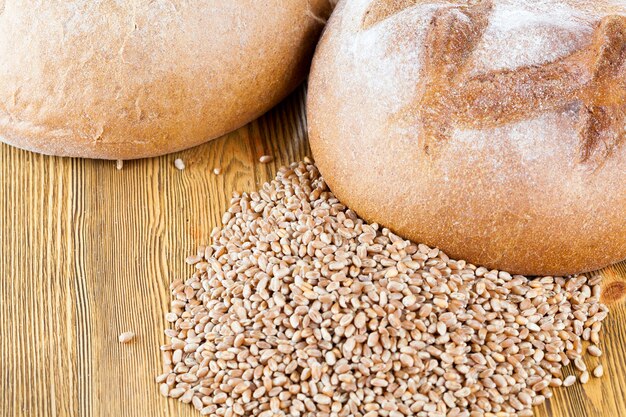 Een brood van volkorenbrood en tarwekorrels gestapeld op een houten tafel, close-up vanaf de bovenkant