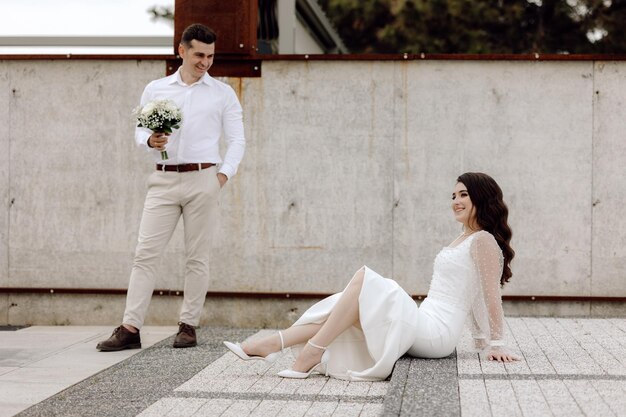 Een bruid en bruidegom zitten op de grond en de man in het witte overhemd draagt een witte jurk en de man in het witte overhemd houdt een boeket bloemen vast.