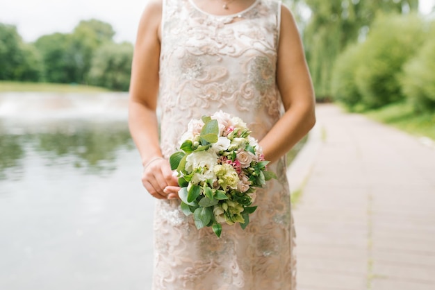 Een bruid in een beige trouwjurk heeft een boeket bloemen en groen in haar handen