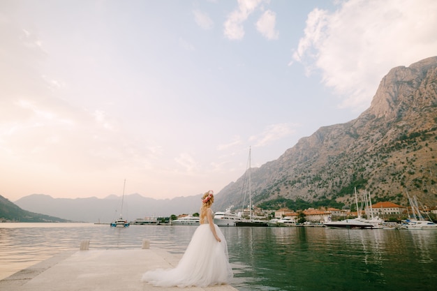 Een bruid in een delicate rozenkrans staat op een pier bij Kotor in de baai van Kotor