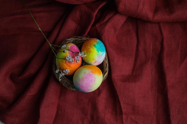 Een bruin nest met veelkleurig beschilderde eieren staat tegen een achtergrond van bordeauxrode stof Paasdecoratie Lente Paasdecor