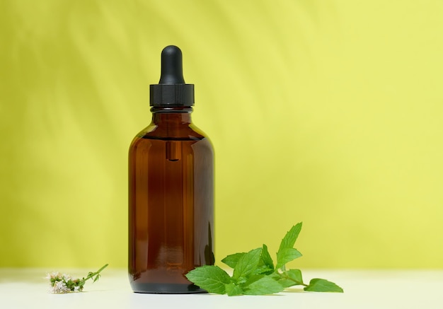 Een bruine glazen fles met een pipet op een groene achtergrond containers voor cosmetica