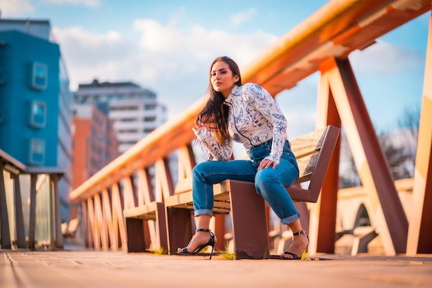Een brunette Latijns meisje in de stad bij zonsondergang op een oranje brug Poseren van de zittende