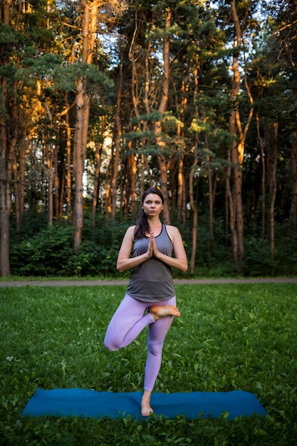 Een brunette meisje doet yoga en voert de Vrikshasana asana uit in de natuur