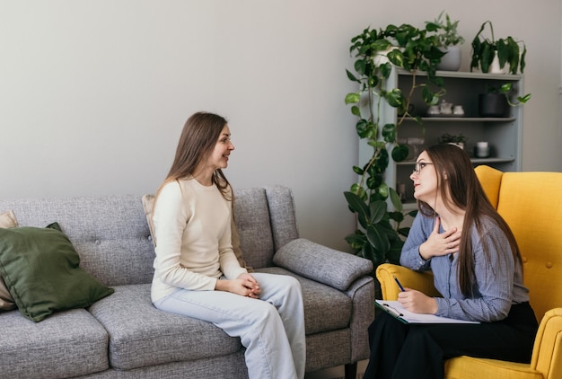 een brunette psycholoog en een vrouwelijke patiënt zitten in een kamer en praten. Een oprecht gesprek. Psychische problemen oplossen