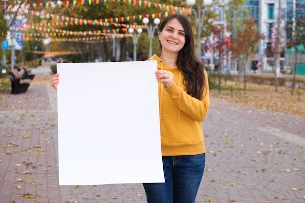 Een brunette vrouw glimlacht en houdt een leeg wit laken vast voor de inscriptie