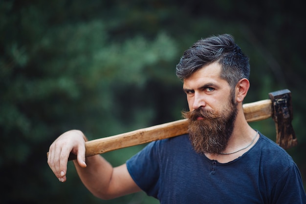 Een brutale bebaarde man van houtbewerkers met een lange baard en snor in een donker T-shirt met een bijl op zijn schouder