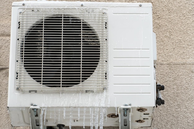 Een buitenairconditionereenheid geïnstalleerd op de buitenmuur van een woongebouwclose-up Werking van de airconditioner in de winter bij lage temperaturen Ijspegels en sneeuw op de airconditioner