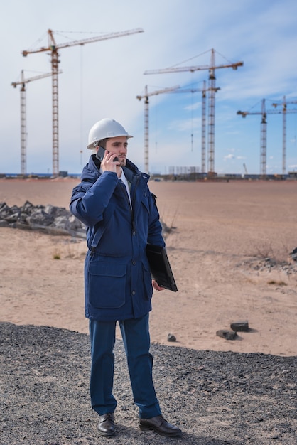 Een burgerlijk ingenieur in een witte helm is in de bouw aan de telefoon.