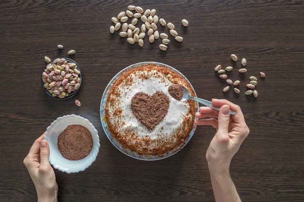 Een cake versieren voor valentijnsdag. met de hand gemaakte pastei met roomkaas het berijpen en een chocoladehart.